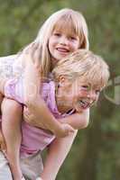 Young boy giving young girl piggyback outdoors smiling