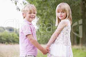 Two young children standing outdoors holding hands smiling