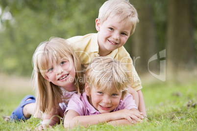 Three young children playing outdoors smiling