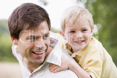 Father giving son piggyback ride outdoors smiling