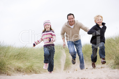 Father and two young children running at beach smiling