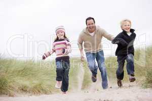 Father and two young children running at beach smiling