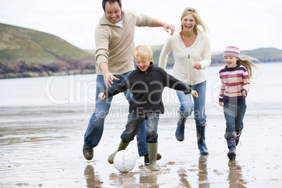 Family playing soccer at beach smiling