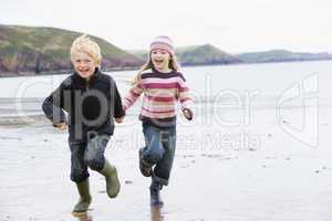 Two young children running on beach holding hands smiling