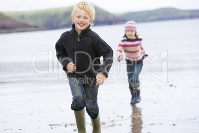 Two young children running on beach smiling