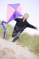 Young boy running on beach with kite smiling