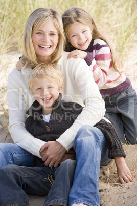 Mother and two young children sitting on beach smiling