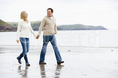 Couple walking on beach holding hands smiling