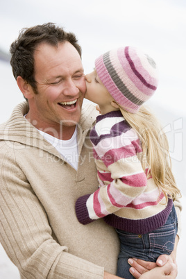 Father holding daughter kissing him at beach smiling