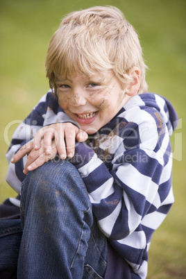 Young boy sitting outdoors dirty and smiling