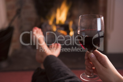 Feet warming at fireplace with hand holding wine