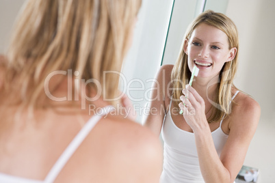 Woman in bathroom brushing teeth smiling