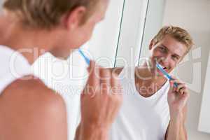 Man in bathroom brushing teeth and smiling