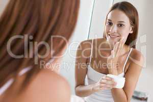 Woman in bathroom applying face cream smiling