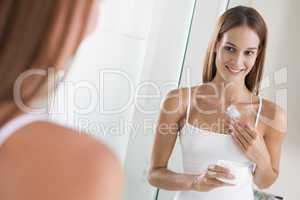 Woman in bathroom applying lotion smiling