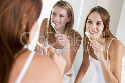 Two women in bathroom brushing teeth and smiling