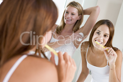 Two women in bathroom brushing teeth applying deodorant and smil