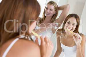 Two women in bathroom brushing teeth applying deodorant and smil