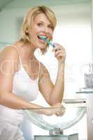 Woman in bathroom brushing teeth smiling