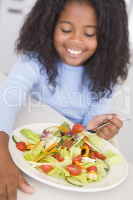 Young girl in kitchen eating salad smiling