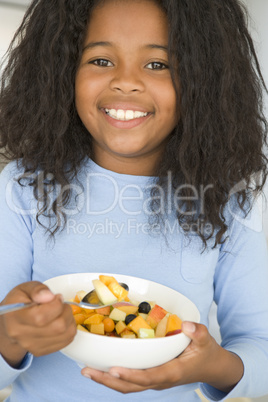 Young girl in kitchen eating bowl of fruit smiling