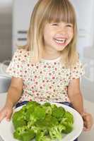 Young girl in kitchen eating broccoli smiling