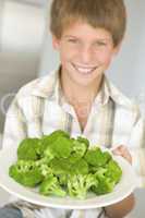 Young boy in kitchen eating broccoli smiling