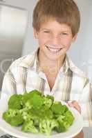 Young boy in kitchen eating broccoli smiling