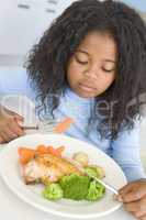 Young girl in kitchen eating chicken and vegetables