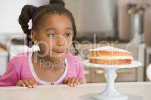 Young girl in kitchen looking at cake on counter