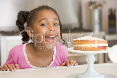 Young girl in kitchen looking at cake on counter smiling