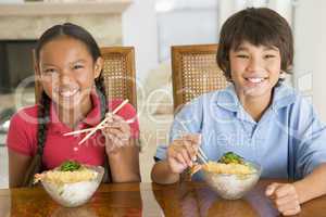 Two young children eating Chinese food in dining room smiling