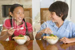 Two young children eating Chinese food in dining room smiling