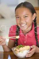 Young girl in dining room eating Chinese food smiling