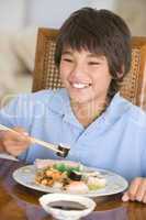 Young boy in dining room eating chinese food smiling