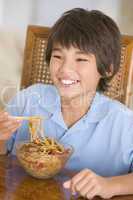 Young boy in dining room eating chinese food smiling