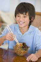 Young boy in dining room eating chinese food smiling