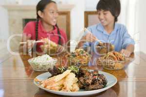 Two young children eating chinese food in dining room smiling