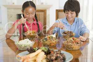 Two young children eating chinese food in dining room smiling