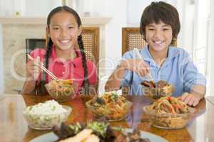 Two young children eating chinese food in dining room smiling