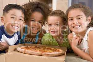 Four young children indoors with pizza smiling