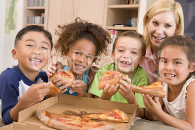 Four young children indoors with woman eating pizza smiling