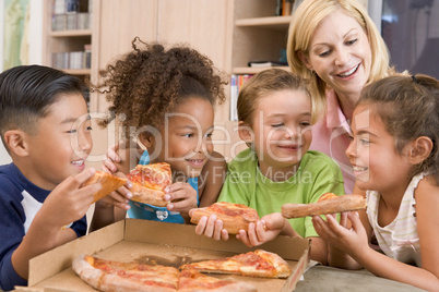 Four young children indoors with woman eating pizza smiling