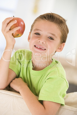 Young boy eating apple in living room smiling