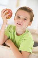 Young boy eating apple in living room smiling