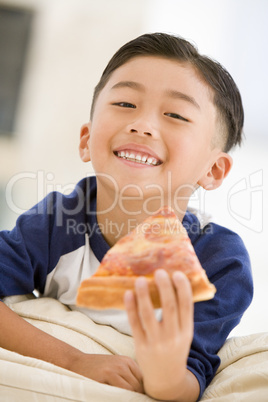 Young boy eating pizza slice in living room smiling