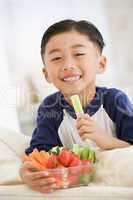 Young boy eating bowl of vegetables in living room smiling