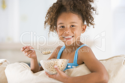 Young girl eating cereal in living room smiling