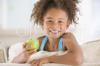 Young girl eating apple in living room smiling