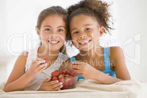 Two young girls eating strawberries in living room smiling